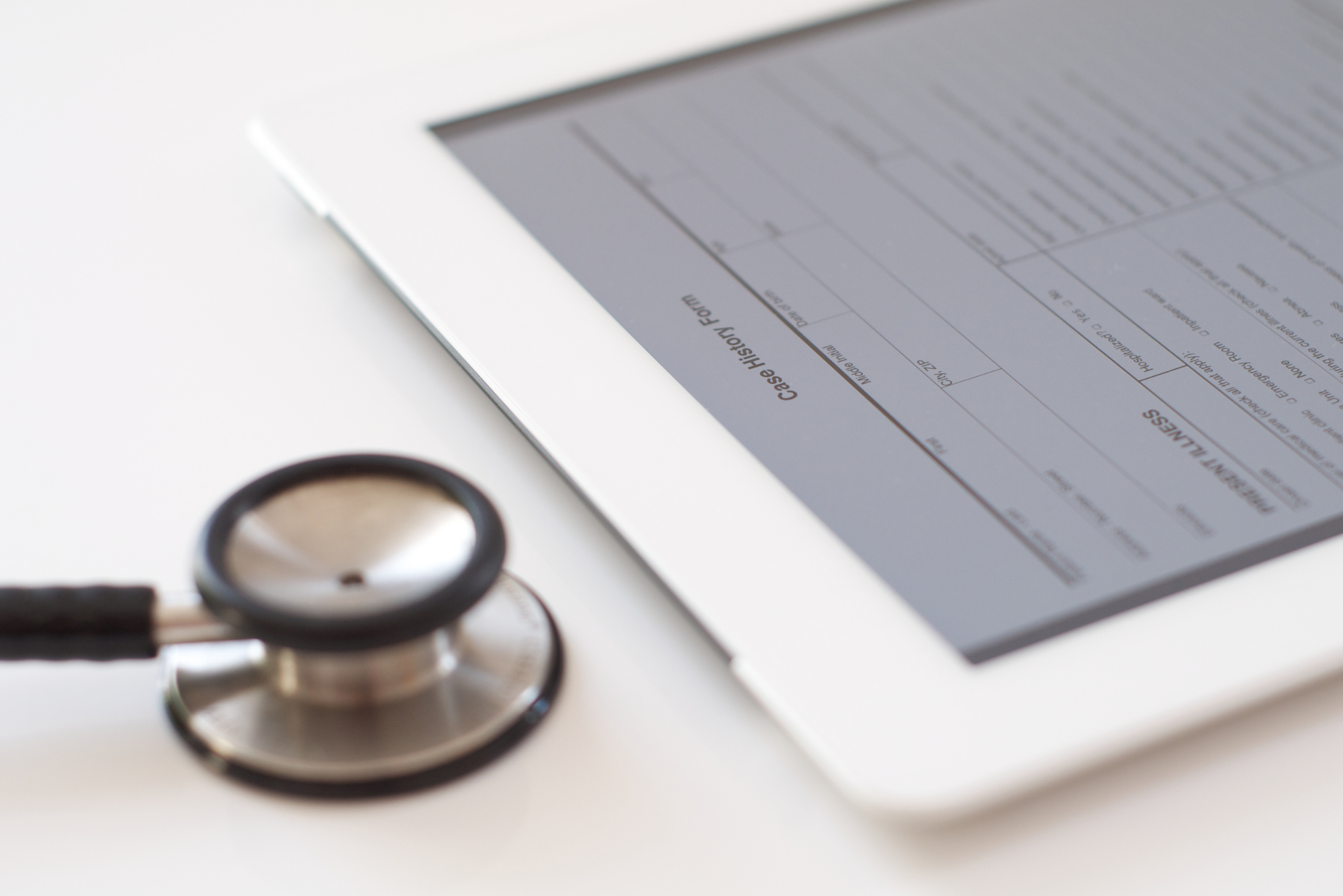 A stethoscope sits next to a tablet with a digital patient form pulled up on the screen.